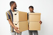 © SHOTPRIME STUDIO - Two African American men smiling while carrying cardboard boxes, showcasing teamwork and camaraderie in a bright and minimalistic setting.