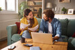 © Stockphotodirectors - A couple sits together on their couch discussing various life insurance plans. They review important documents while a laptop is open on the coffee table, creating a warm atmosphere.