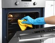 © ImagePulse - A person wearing a blue glove cleans the inside of a modern oven with a yellow cloth.