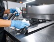 © ImagePulse - A person wearing blue gloves cleans a stainless steel stove with a spray bottle and cloth in a commercial kitchen.