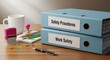 © Izdihaar - Two blue binders labeled 'Safety Procedures' and 'Work Safety' sit on a desk with a mug, pens, stamps, and paperclips.