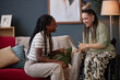 © Seventyfour - Young adult Black woman sitting on sofa laughing with young adult Caucasian woman with disability in wheelchair, both smiling and gesturing while enjoying friendly conversation indoors