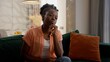 © Yuliia - Pondering pensive thoughtful African American ethnic woman puzzled female model lady homeowner client thinking touching chin deep thoughts solving problem solution sitting couch indoors at home room