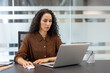 © Liubomir - A woman with curly hair works on a laptop in an office setting, focusing intently on her computer screen.