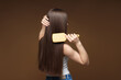 © New Africa - Teenage girl brushing her healthy long hair on brown background