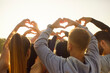 © Studio Romantic - Friends group making heart shape gesture with fingers in sunlight. Happy people raise hands to sun outdoor, greeting orange sunset or sunrise with love. Gratitude to nature, freedom, hope concept