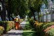 © Audrey - Worker trimming grass along the sidewalk in a sunny urban park during the afternoon