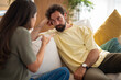 © Dexon Dee - Young couple sitting on a sofa during a serious conversation. The woman is pointing while the man listens with a thoughtful and slightly emotional expression in a cozy home setting.