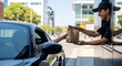 © Niko - Drive-through service: a smiling male employee in a cap hands a paper bag with food to a customer in a dark car at a fast food restaurant or cafe.