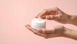 © Dreamera - Mano aplicando crema hidratante blanca sobre fondo rosado pastel con textura cremosa visible en primer plano