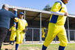 © Wavebreak Media - Diverse male baseball players in yellow jerseys high-fiving coach while holding glove near dugout