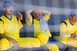© Wavebreak Media - Senior male baseball teammates sitting in dugout wearing yellow uniforms through fence shadows