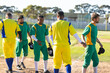 © Wavebreak Media - Diverse male baseball players shaking hands on dirt infield at community park while holding caps