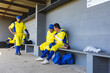 © Wavebreak Media - Male baseball players sitting in dugout in yellow and blue uniforms, talking and holding gloves