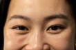 © Wavebreak Media - Asian woman presenting skin texture and defined eye area under warm lighting against dark backdrop