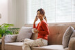 © David - Relax Concept. Happy asian woman drinking coffee holding phone call  sitting on comfortable couch at home. dreaming Cheerful casual famale resting on sofa, enjoying weekend free time.