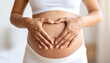 © vinka - Close Up of Pregnant Belly with Hands Making Love Heart, Indoor with White Shirt