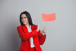 © deagreez - Businesswoman in a red suit holding a red flag while making a gesture against the concept, on a neutral grey background