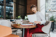 © qunica.com - A professional woman in business attire reviews documents while seated in a contemporary cafe environment, exemplifying focus and efficiency in her entrepreneurial endeavors.