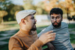© qunica.com - Two men engage in a lively discussion while sitting on a park bench under the sun. The setting features greenery and a relaxed outdoor atmosphere, highlighting friendship and connection.