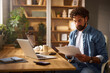 © Stockphotodirectors - A man engages in work tasks using a laptop and reviewing documents in a well-lit home office. The atmosphere is organized and inviting, showcasing a productive space.