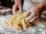 Hands making fresh homemade pasta on a floured countertop