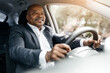 © Anastasiya - Black businessman driving car and smiling while holding steering wheel, hands firmly positioned. Calm and composed driver dressed for success, closeup