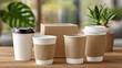 © Chisanu - Disposable coffee cups with cardboard sleeves and cardboard box on wooden table with green plants in background