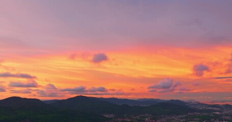 Wall Mural - A breathtaking sunset paints the sky in vivid hues of orange and blue over a coastal town, with lush green hills framing the scene. A distant hilltop structure adds a serene focal point 