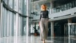 © CStock - Confident woman walking through a modern office space, showcasing contemporary professional style and architecture.