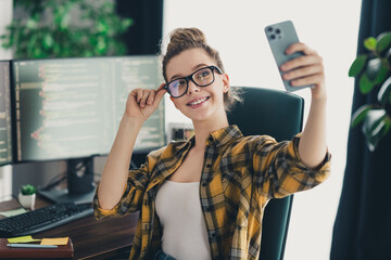 young programmer taking a photo with her phone in a modern workspace, surrounded by computer screens