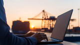 Sunset Work: Man typing on laptop with cargo ship and cranes at harbor during beautiful sunset. Business on the go with technology at a busy port.