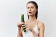 © SHOTPRIME STUDIO - surprised young woman holding cucumber, shocked expression standing against plain white background Natural beauty concept with fresh vegetables, healthy lifestyle and humor