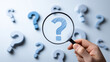 © GreenOptix - Hand holding magnifying glass over central question mark surrounded by smaller question marks on white background. Symbolizes critical thinking and problem-solving