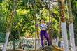 © Daniel Ching - Woman in striped shirt and purple leggings holding phone and standing among lush trees in rural hotel setting of Santuario, Risaralda, Colombia beside tropical river.