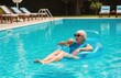 © Vadym - Cheerful woman on inflatable in pool with drink in hand soaking up summer rays on peaceful resort day