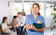 © JackF - Polite young female therapist in blue uniform standing in clinic, filling clipboard with medical records..