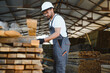 © Serhii - Carpenter checking lumber in warehouse, woodworking industry professional at work