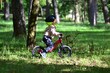 © Karolina - Little boy in helmet riding red balance bike among trees in green park. Side view captures focus, curiosity, and joy of outdoor adventure, highlighting active childhood lifestyle and nature connection