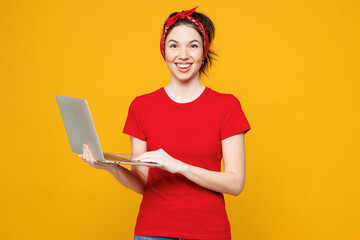 Young smiling happy smart fun IT woman she wearing red t-shirt casual clothes hold use work on laptop pc computer looking camera isolated on plain yellow background studio portrait. Lifestyle concept.
