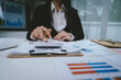 © Kieng - A professional businesswoman calculates financial data using a calculator, surrounded by charts and reports, analyzing company performance to ensure growth, profitability, and strategic business decis