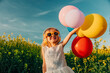 © Westend61 - Girl in a white dress holding colorful balloons in a rapeseed field on a sunny day