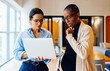 © (JLco) Julia Amaral - Two professionals working together discussing information on a laptop in an office