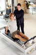 © Georgii - Trainer guiding a client during a Pilates session on a reformer machine