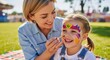 © Meow Creations - Happy mother applying colorful face paint to her joyful young daughter at an outdoor event