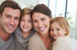 © Helena - Smiling family of four, including two children, posing together in a bright living room, showcasing love and connection in a warm, inviting atmosphere