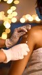© Fcdua - Close-up of a vaccination.  Gloved hands administer a shot in the upper arm, covered with a bandage.  Bokeh lights in the background