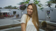 © Krakenimages.com - Woman smiling outdoors in a sunny courtyard with greenery and white architecture in a peaceful setting.