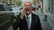 © Krakenimages.com - Senior man in a suit laughing joyfully on a bustling street, surrounded by cars and people in an outdoor urban setting.