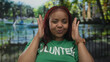 © Krakenimages.com - Woman framing face with hands wearing green volunteer shirt by metal fence and lake in forest; joy playfulness.